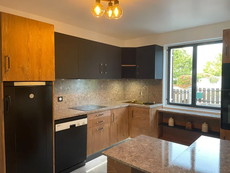 Cuisine après rénovation clé en main à Orléans : meubles noirs et bois, plan de travail effet terrazzo et suspension dorée